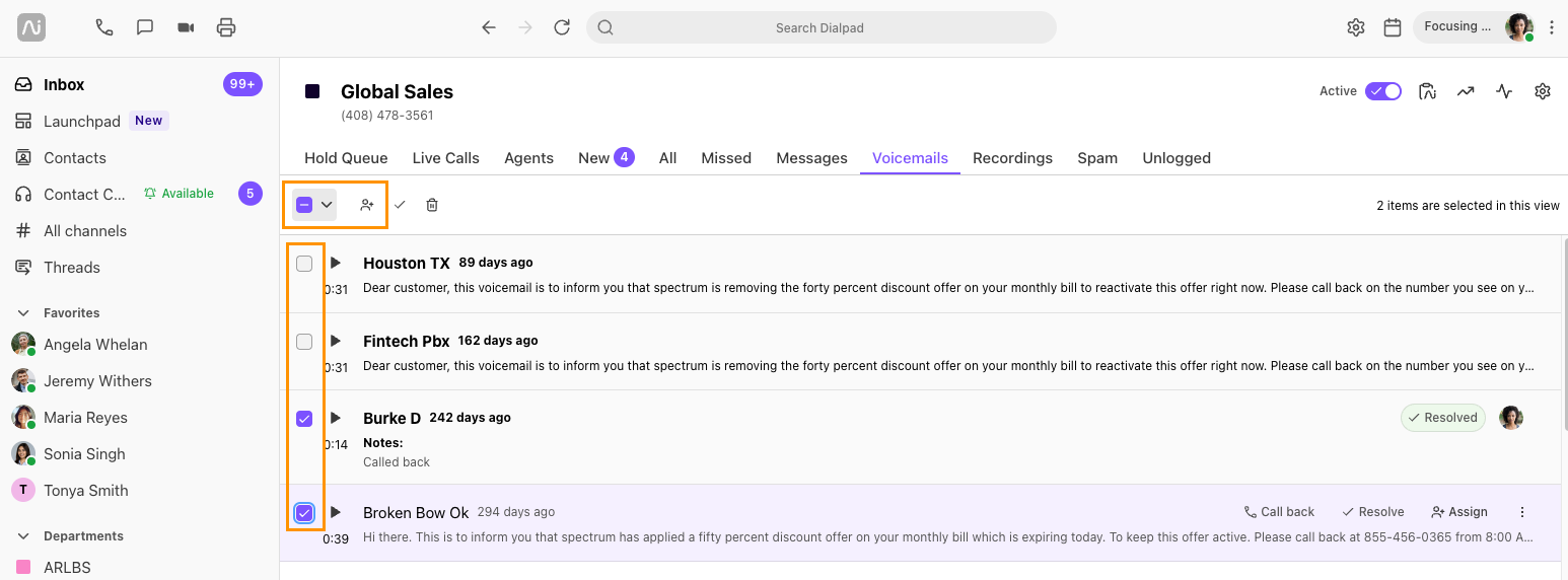 Screenshot of Dialpad open to the Voicemails tab, showing two selected voicemails with orange boxes highlighting the selection checkboxes on the left and the top bulk assignment control button.