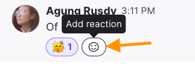 Screenshot of an existing emoji reaction beneath a chat message with an orange arrow pointing to the smiley face 'Add reaction' icon next to it.